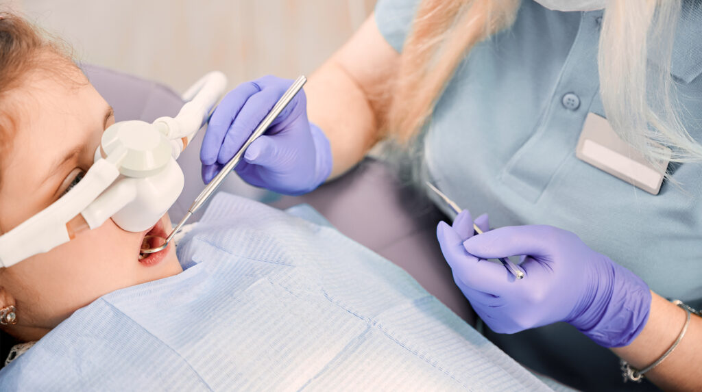 child with laughing gas mask on having teeth examined with sedation dentistry